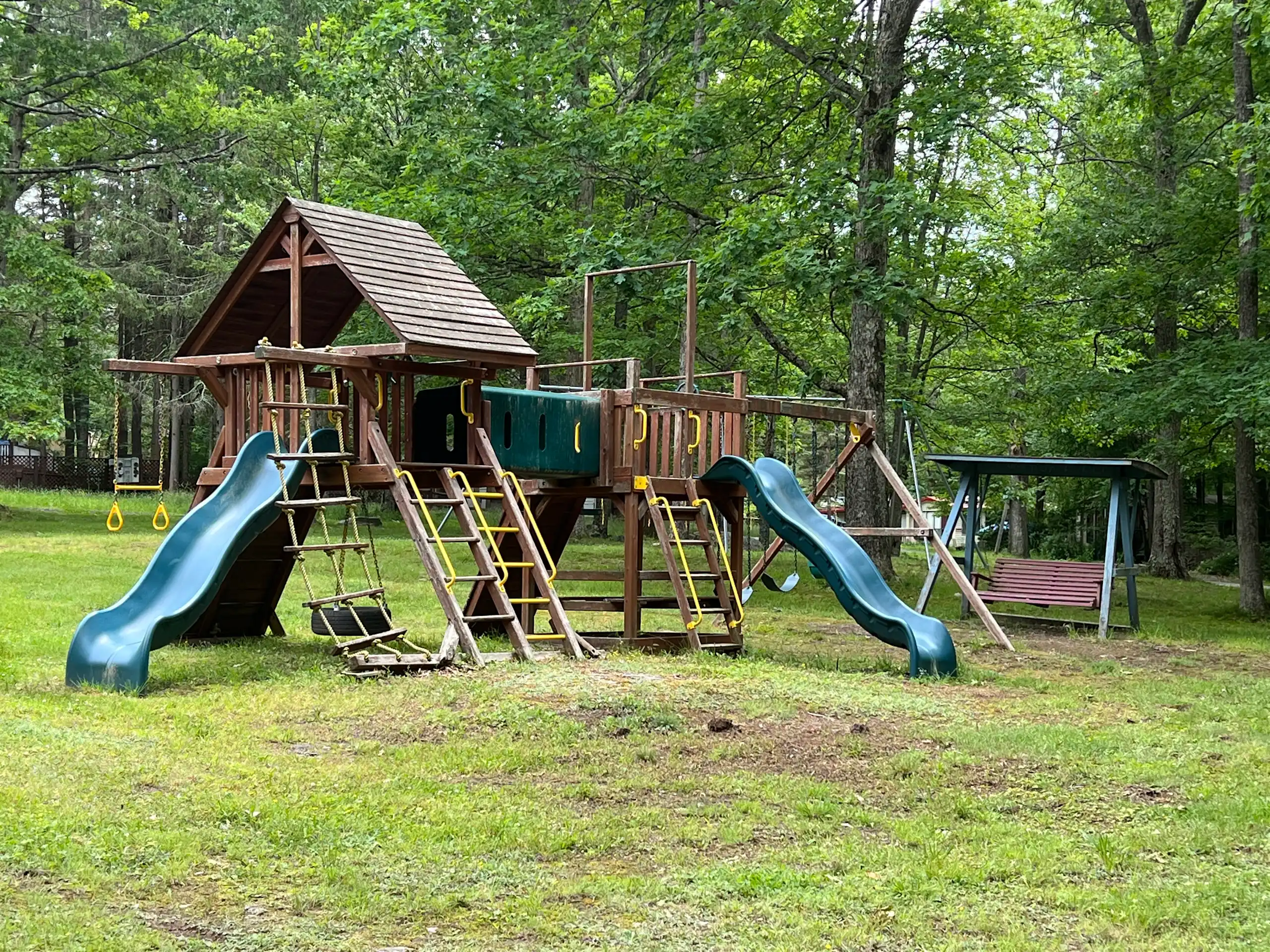 Wooden playground with slides, swings, and climbing areas surrounded by trees at Big Bear Private Community in the Poconos.